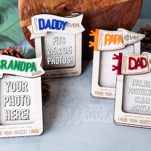May include: Four wooden photo frames with different designs and text. Each frame has a banner with the words "Best" and a title like "Grandpa", "Daddy", "Papa", or "Dad" followed by "ever". The frames are designed to hold 2.5 x 3.5 inch photos. The frames are made by 303 Woods.