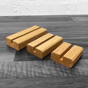 Puede incluir: Tres expositores de madera de diferentes tama&ntilde;os, cada uno con una ranura cortada para sostener tarjetas u otros art&iacute;culos peque&ntilde;os. Los expositores est&aacute;n hechos de madera natural y tienen un color marr&oacute;n claro.