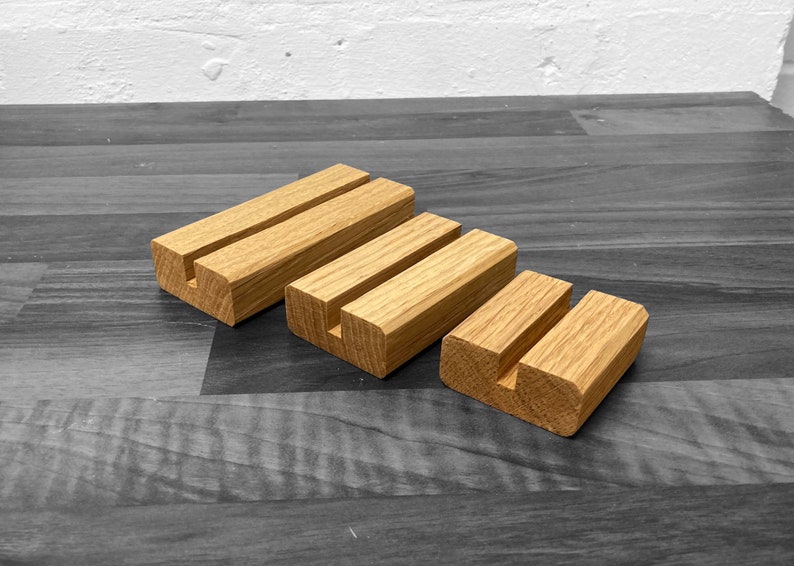 Puede incluir: Tres expositores de madera de diferentes tama&ntilde;os, cada uno con una ranura cortada para sostener tarjetas u otros art&iacute;culos peque&ntilde;os. Los expositores est&aacute;n hechos de madera natural y tienen un color marr&oacute;n claro.