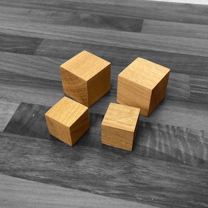 May include: Four wooden cubes of varying sizes, arranged on a dark wood surface. The cubes are made of natural wood with a light brown colour.