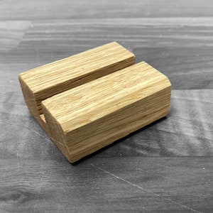 Puede incluir: Un soporte de tel&eacute;fono de madera con un acabado natural. El soporte tiene una ranura en el centro para sostener un tel&eacute;fono en posici&oacute;n vertical.