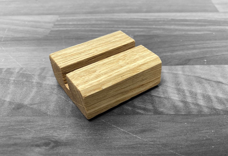 Puede incluir: Un soporte de tel&eacute;fono de madera con un acabado natural. El soporte tiene una ranura en el centro para sostener un tel&eacute;fono en posici&oacute;n vertical.