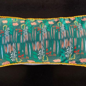 May include: A green pillow with a floral pattern featuring pink, orange, and white flowers. The pillow has a yellow border and a white backing.