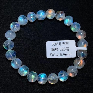 May include: A circular bracelet composed of translucent, spherical moonstone beads that exhibit a blue and orange iridescent sheen. A white rectangular tag is attached to the beads, featuring the text: 天然月光石, 编号:E25号, 约8.4-8.9mm.
