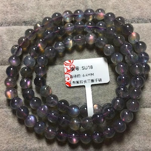 May include: A strand of iridescent purple gemstone beads. The beads are round and appear to be made of a translucent material. A white tag with Chinese characters is attached to the strand. The beads are approximately 6.4 mm in diameter.