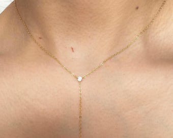 Puede incluir: Un delicado collar tipo lariat en oro con una cadena fina, una piedra redonda transparente de talla brillante en la unión central y una piedra transparente de talla marquesa que cuelga al final de la cadena vertical en forma de Y.