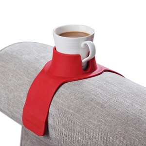 May include: Red silicone couch cup holder with a white ceramic mug filled with coffee. The holder has the text "Couch Cozie" printed on it.