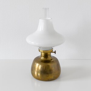 May include: A brass oil lamp with a white glass shade. The lamp has a round base and a simple design.