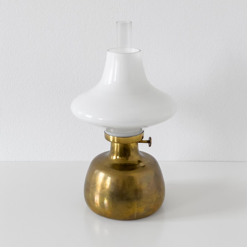 May include: A brass oil lamp with a white glass shade. The lamp has a round base and a simple design.