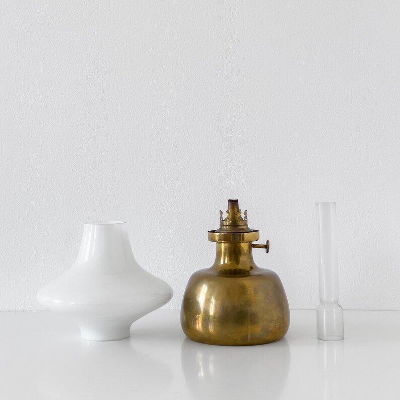 May include: A brass oil lamp with a white glass shade and a clear glass chimney. The lamp is on a white surface.