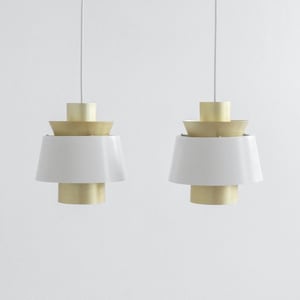 May include: Two white and gold pendant lights with a layered design. The lights are hanging from white cords against a white wall.