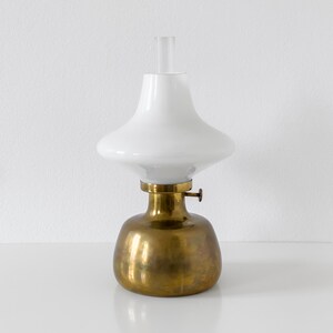May include: A brass and white oil lamp with a round base and a white glass shade. The shade has a wide, flat top and a narrow, pointed bottom.
