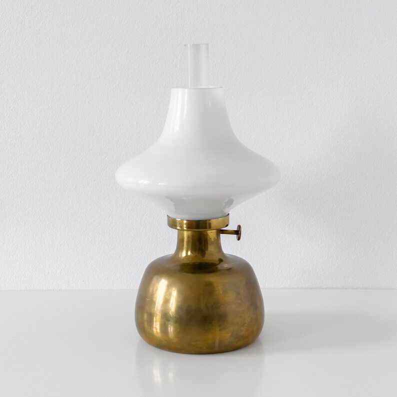 May include: A brass and white oil lamp with a round base and a white glass shade. The shade has a wide, flat top and a narrow, pointed bottom.