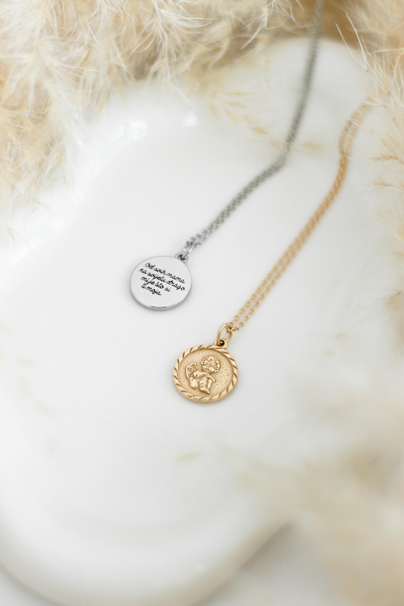 Op de afbeelding: Twee zilveren kettingen met hangers. Een hanger is een ronde schijf met de tekst "Did your mama ever tell you to never let go of your dreams" erop. De andere hanger is een ronde schijf met een gouden cherub-engelmotief.