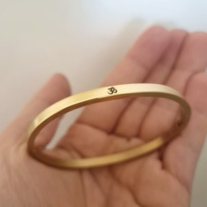 Puede incluir: Un brazalete de oro con un simple símbolo Om grabado en la parte delantera.
