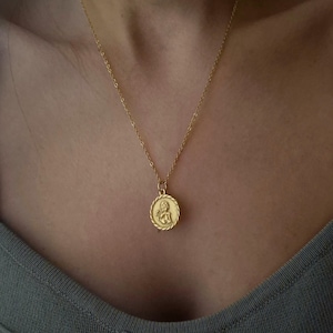 Op de afbeelding: Een gouden ketting met een ronde hanger met een cherub-ontwerp.
