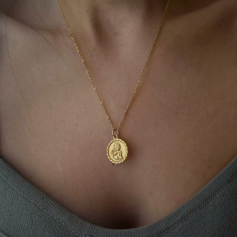 Op de afbeelding: Een gouden ketting met een ronde hanger met een cherub-ontwerp.