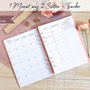 Könnte beinhalten: Ein rosa A5 (14,8 x 21 cm) Monats-Planer mit gepunktetem Raster. Der Planer hat eine Ringbindung und beinhaltet einen Tracker-Bereich für den Monat Februar. Der Planer ist auf Januar 2023 geöffnet und zeigt die Wochentage auf Deutsch.