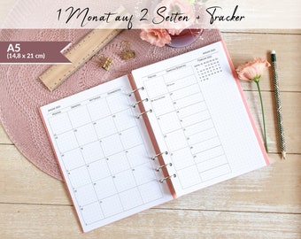 May include: A pink A5 (14.8 x 21 cm) monthly planner with a dotted grid layout. The planner has a ring binding and includes a tracker section for the month of February. The planner is open to January 2023, showing the days of the week in German.