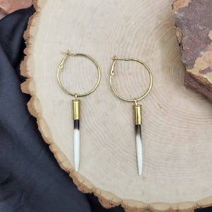 May include: A pair of gold hoop earrings with a long, white and brown,  bullet-shaped pendant hanging from each hoop.