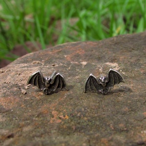 Op de afbeelding: Een paar zilveren vleermuis oorbellen. De vleermuizen kijken naar voren met hun vleugels uitgespreid.