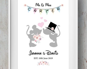 May include: A white framed print with a silhouette of Mickey and Minnie Mouse kissing. The print has a pink, blue, and yellow bunting with the text "Mr & Mrs CARTER" above the mice. The text "Joanna & David EST. 10th June 2019" is below the mice.