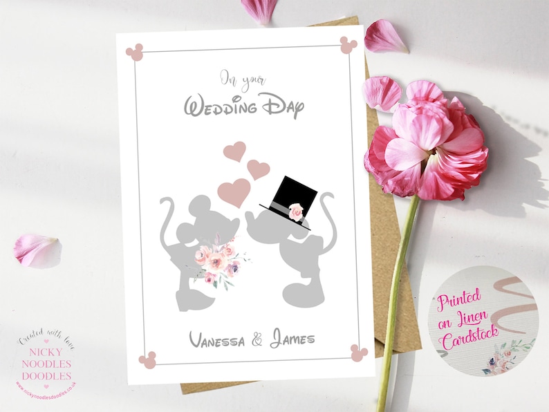 May include: A white card with a gray silhouette of Mickey and Minnie Mouse kissing. The card has the text "On your Wedding Day" and "Vanessa & James" printed on it. The card is decorated with pink hearts and flowers.