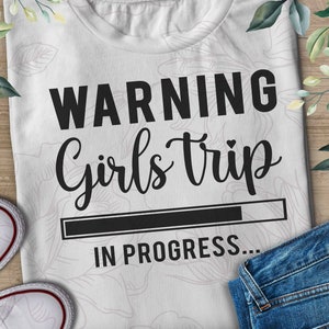 May include: White t-shirt with black text that reads "WARNING Girls Trip IN PROGRESS..."  The text is in a handwritten font.