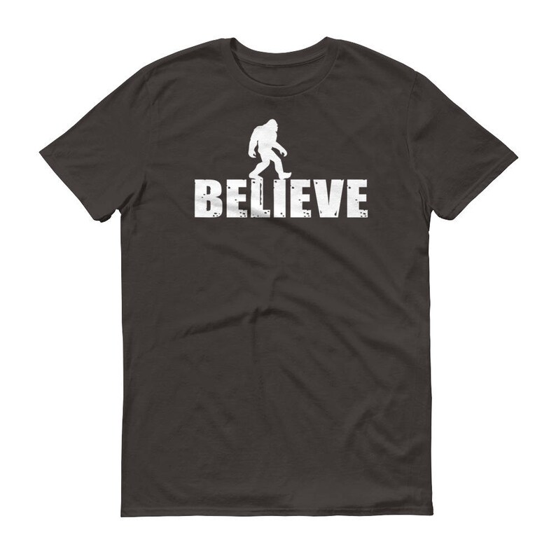 May include: Dark gray t-shirt with a white silhouette of Bigfoot walking and the text "BELIEVE" underneath.