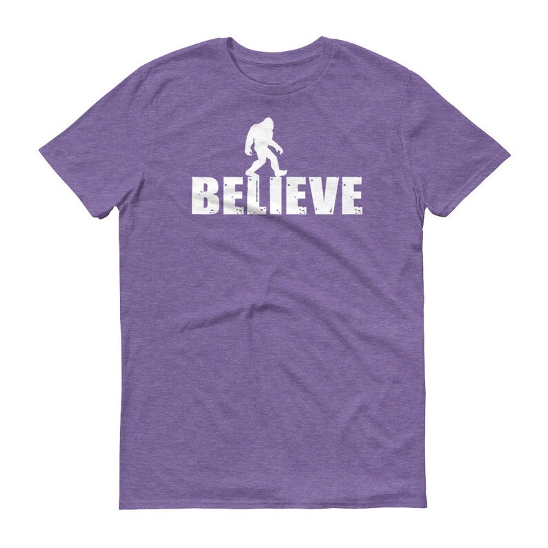 May include: Purple t-shirt with a white silhouette of Bigfoot walking and the word "BELIEVE" printed below.