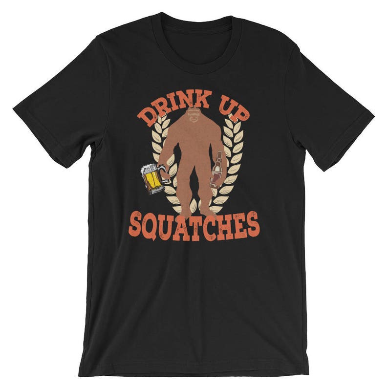 May include: Black t-shirt with a graphic of a Bigfoot holding a beer and a bottle. The text "Drink Up Squatchies" is printed in orange on the shirt.