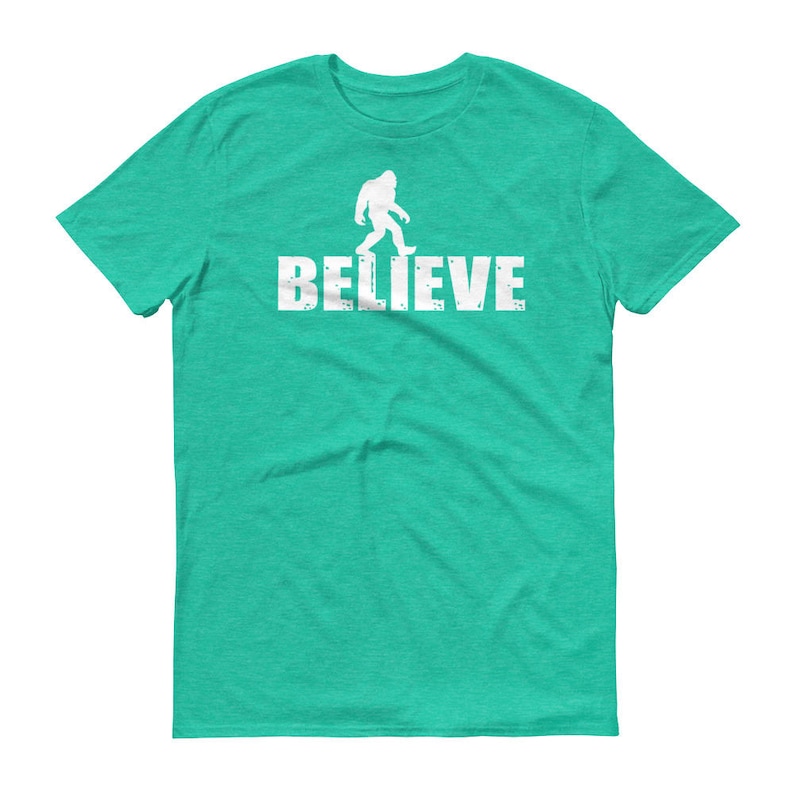 May include: A teal blue t-shirt with a white silhouette of Bigfoot walking and the word "BELIEVE" printed below it.