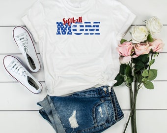 May include: White t-shirt with a red and blue graphic that says "Softball Mom" with a distressed American flag design.