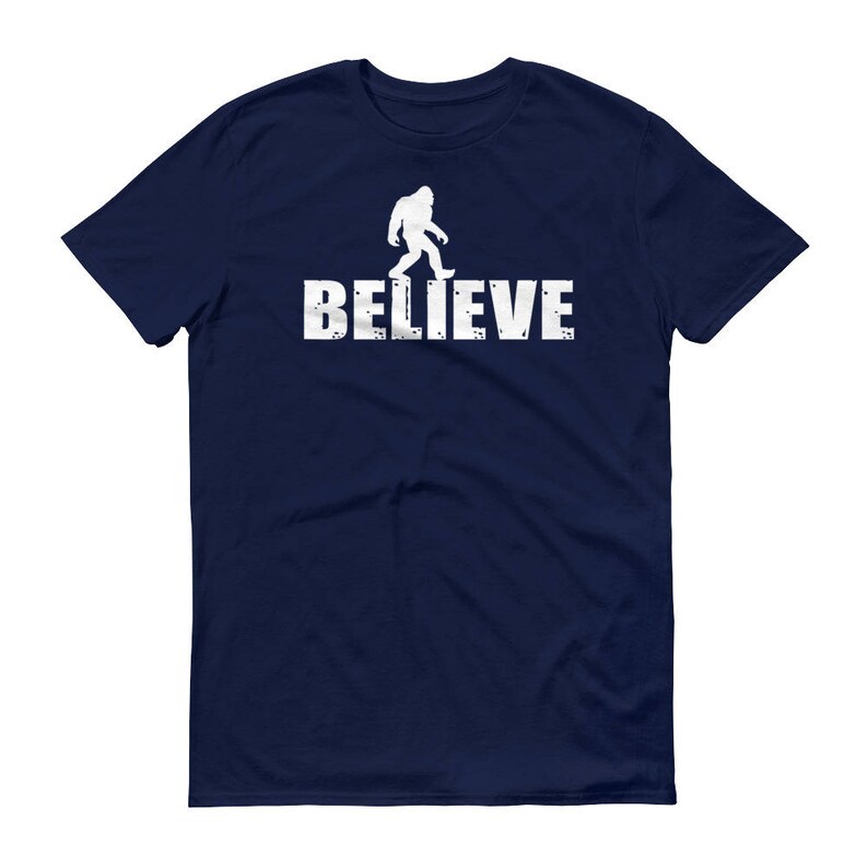 May include: A navy blue t-shirt with a white silhouette of Bigfoot walking and the word "BELIEVE" printed below it.