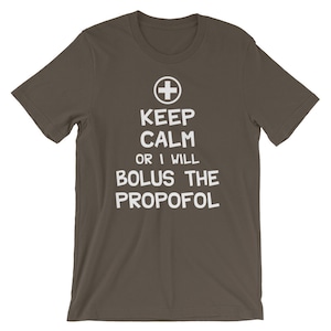 Puede incluir: Una camiseta marr&oacute;n oscuro con texto blanco que dice "Keep Calm or I Will Bolus the Propofol". Un s&iacute;mbolo de cruz m&eacute;dica est&aacute; por encima del texto.