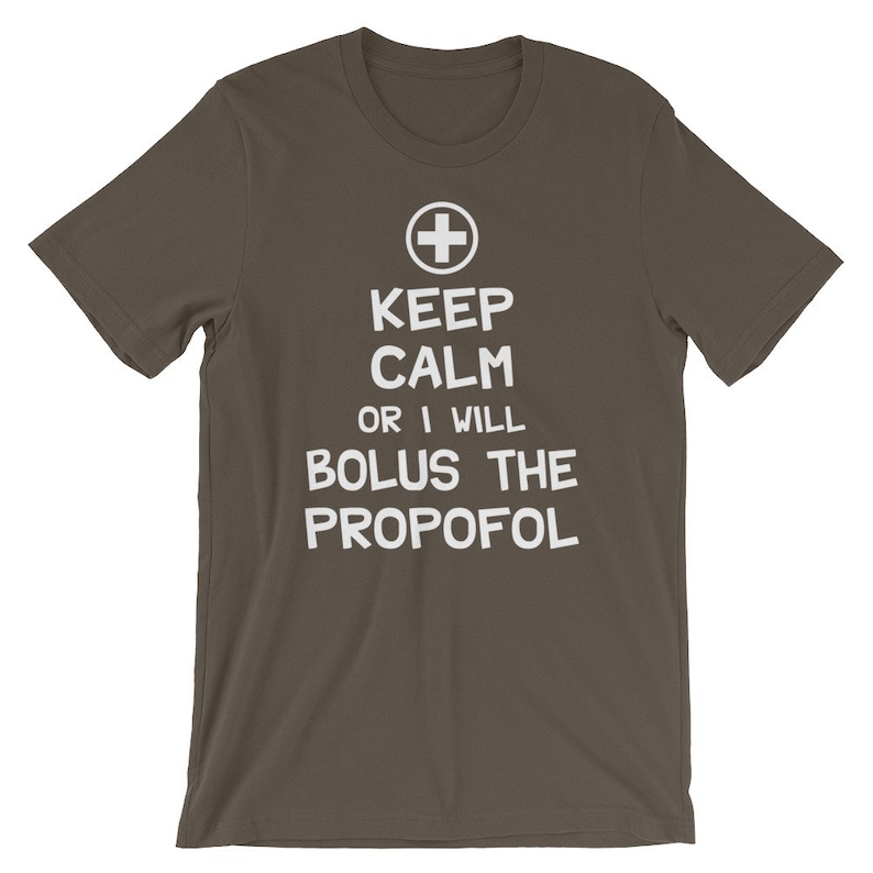 Puede incluir: Una camiseta marr&oacute;n oscuro con texto blanco que dice "Keep Calm or I Will Bolus the Propofol". Un s&iacute;mbolo de cruz m&eacute;dica est&aacute; por encima del texto.