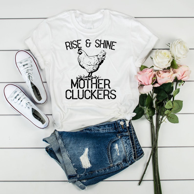 May include: White t-shirt with a black and white illustration of a chicken and the text "Rise & Shine Mother Cluckers".