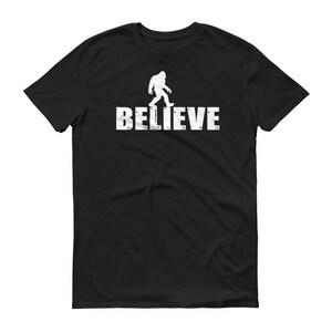 May include: Black t-shirt with a white silhouette of Bigfoot walking and the word "BELIEVE" printed below.