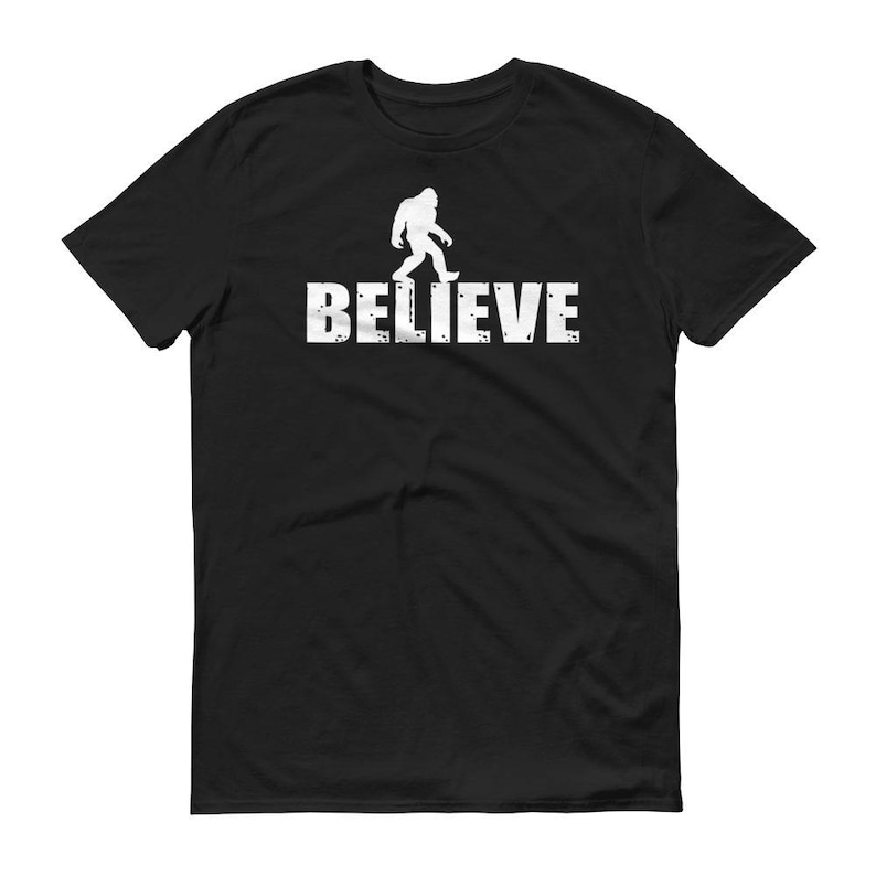 May include: Black t-shirt with a white silhouette of Bigfoot walking and the word "BELIEVE" printed below.