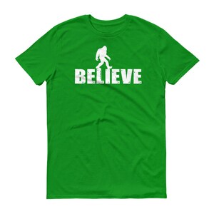 May include: A green t-shirt with a white silhouette of Bigfoot walking and the word "BELIEVE" printed on the front.