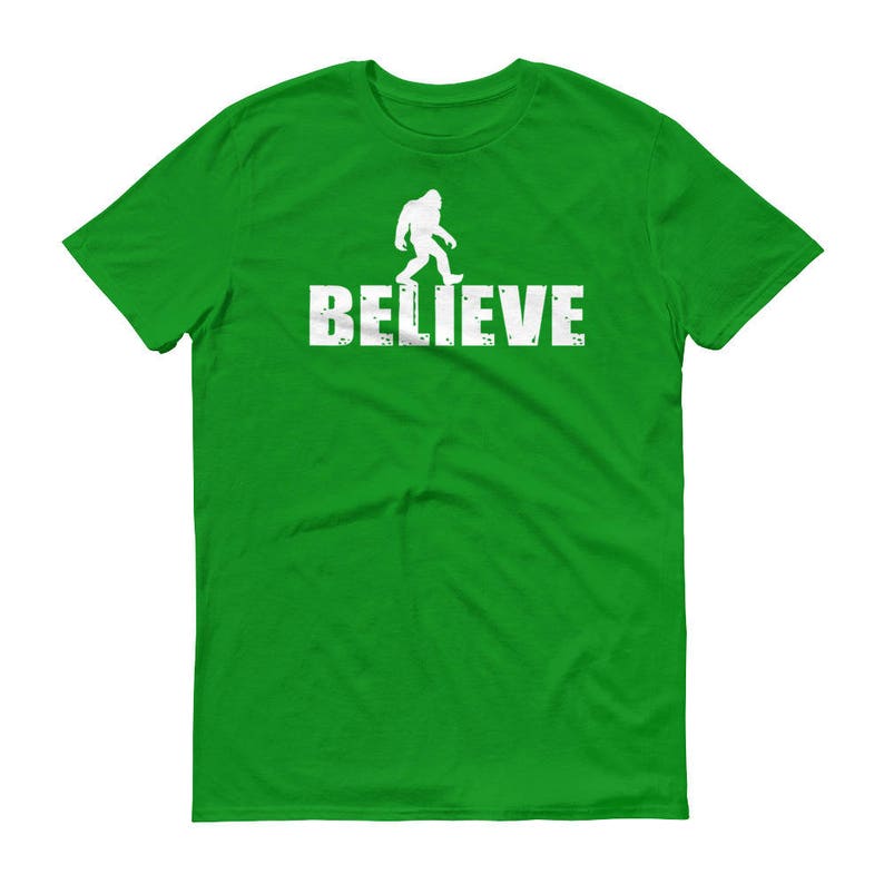 May include: A green t-shirt with a white silhouette of Bigfoot walking and the word "BELIEVE" printed on the front.