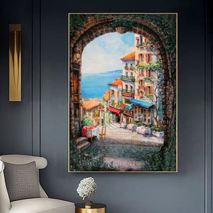 May include: A painting of a colorful, European cityscape viewed through an arched doorway. The scene features buildings with terracotta roofs, balconies, and shops. The sky is blue and the sea is visible in the distance.