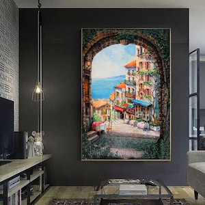 May include: A painting of a colorful, European-style street scene viewed through an arched doorway. The street is lined with buildings and shops, and there are people walking and sitting at tables outside. The scene is painted in a realistic style with vibrant colors.