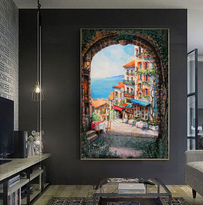 May include: A painting of a colorful, European-style street scene viewed through an arched doorway. The street is lined with buildings and shops, and there are people walking and sitting at tables outside. The scene is painted in a realistic style with vibrant colors.