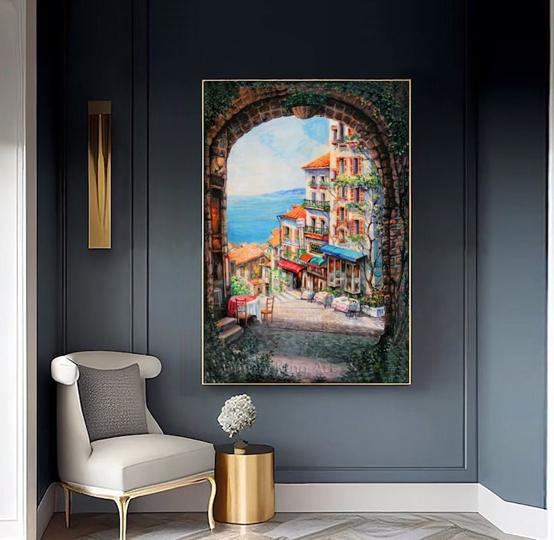 May include: A painting of a colorful, European cityscape viewed through an arched doorway. The scene features buildings with terracotta roofs, balconies, and shops. The sky is blue and the sea is visible in the distance.