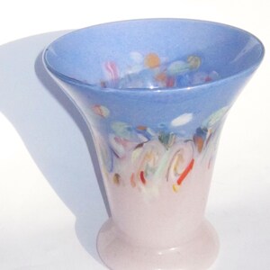May include: A decorative glass vase with a flared top and a rounded base. The top is light blue with colorful abstract designs, while the lower portion is a soft pink. The vase is approximately 7 inches tall.