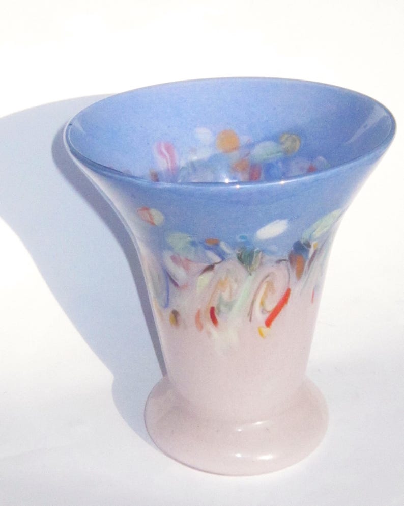May include: A decorative glass vase with a flared top and a rounded base. The top is light blue with colorful abstract designs, while the lower portion is a soft pink. The vase is approximately 7 inches tall.