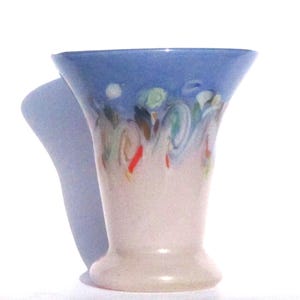 May include: A ceramic vase with a flared top and a pedestal base. The top is painted light blue, with colorful abstract swirls in green, red, and brown. The body of the vase is a creamy white color.