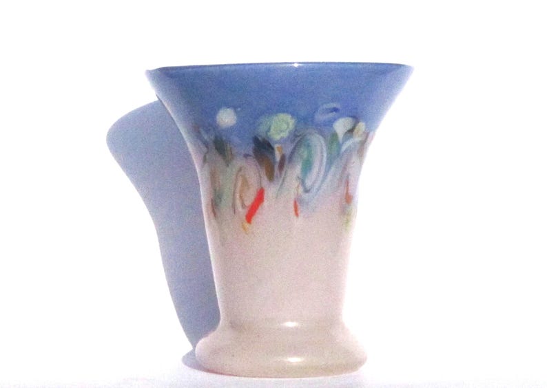 May include: A ceramic vase with a flared top and a pedestal base. The top is painted light blue, with colorful abstract swirls in green, red, and brown. The body of the vase is a creamy white color.