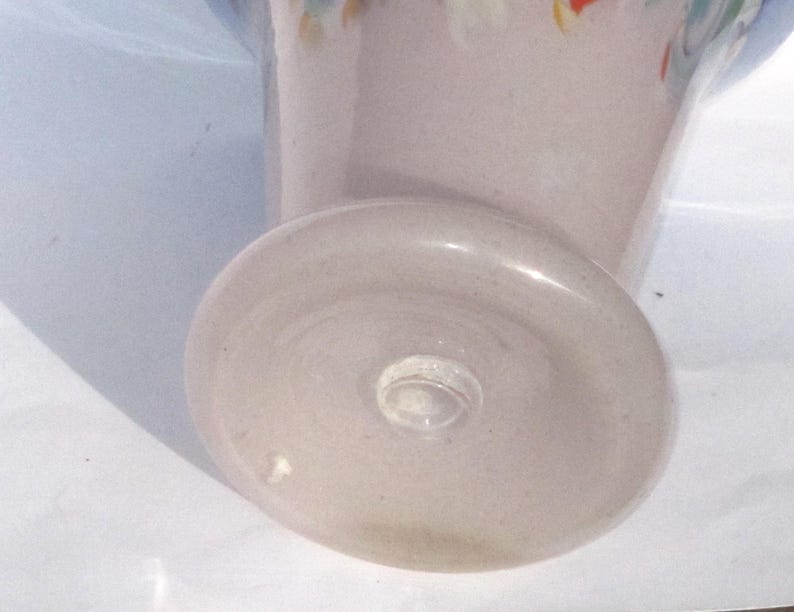 May include: A light pink glass vase with a rounded base and a flared top. The base is approximately 3 inches in diameter. The vase has a clear glass stem and a decorative rim with colorful accents.